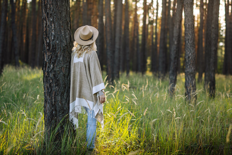 Woman in poncho and hat standing at pine tree and relaxing in forest. Connection and harmony between people and nature - 5 Proven Ways to Calm Your Brain and Stop Stress