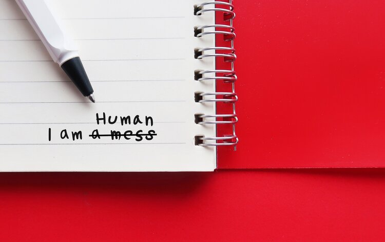 Notebook on red copy space background with handwriting I AM A MESS, changed to I AM HUMAN - to overcome negative self talk or inner voice critic, change to positive thought to boost self esteem - Science Shows Repeated Thoughts Are Powerful Tools to Improve Your Brain